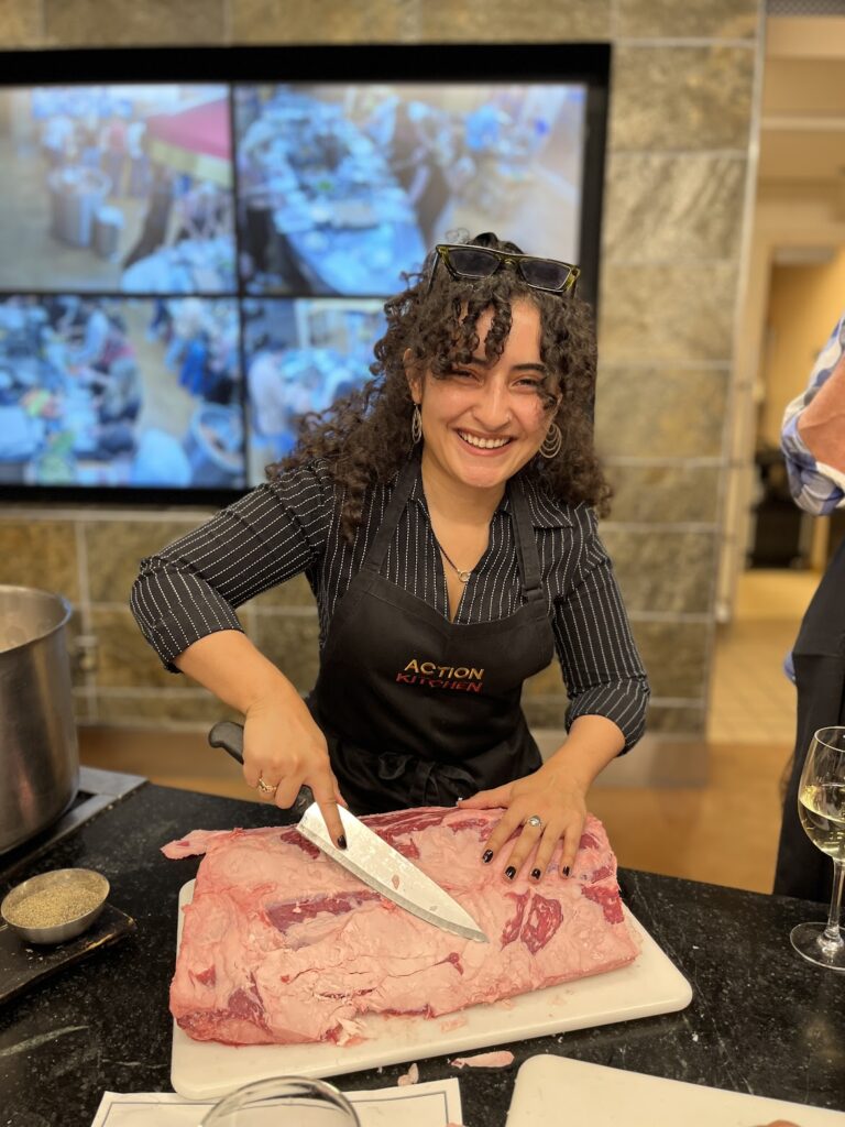 A woman with an apron and a large knife cutting up a piece of meat